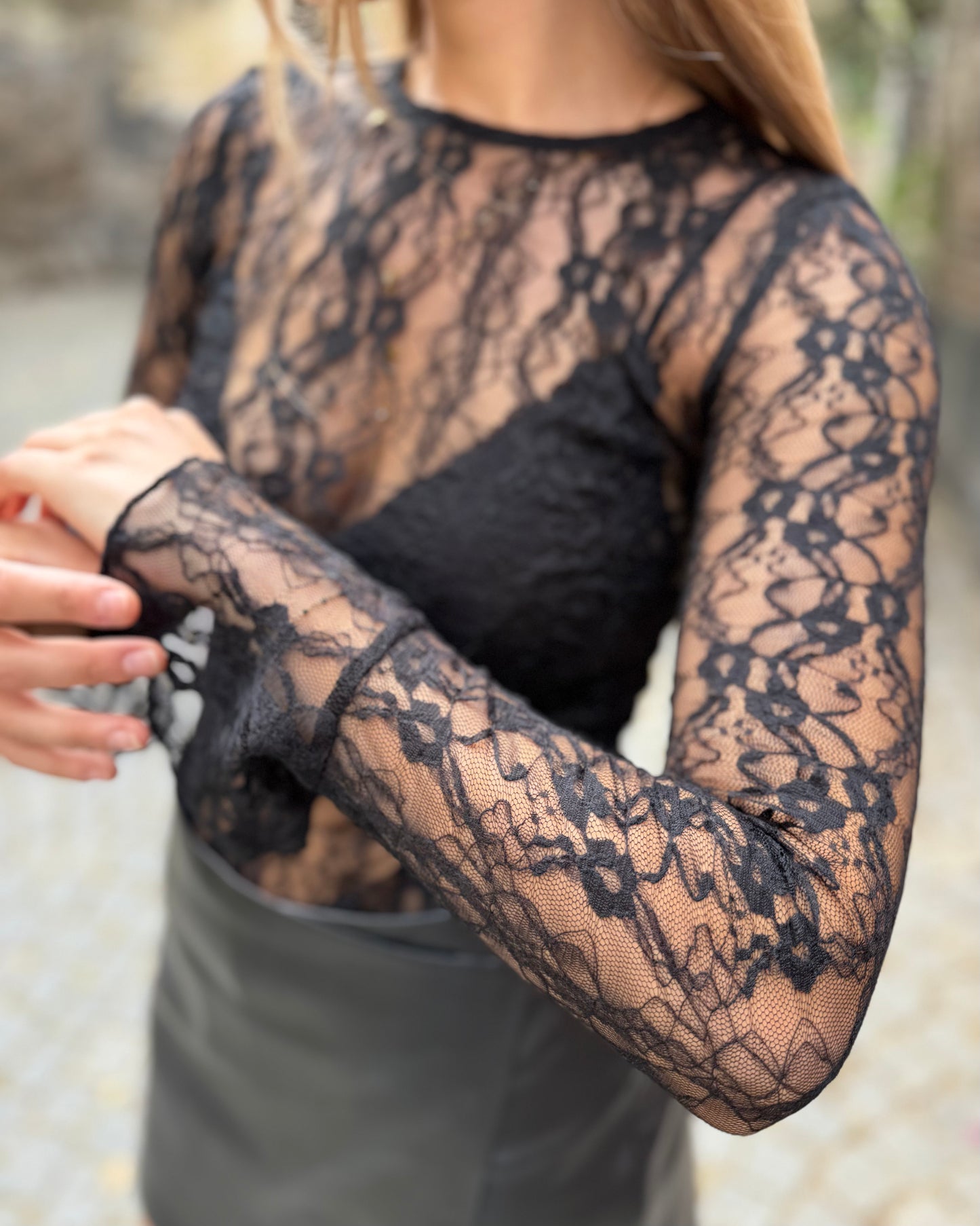 Blouse noire en dentelles légère et transparente. Coupe moulante avec des longues manches évasées et une dentelle florale.