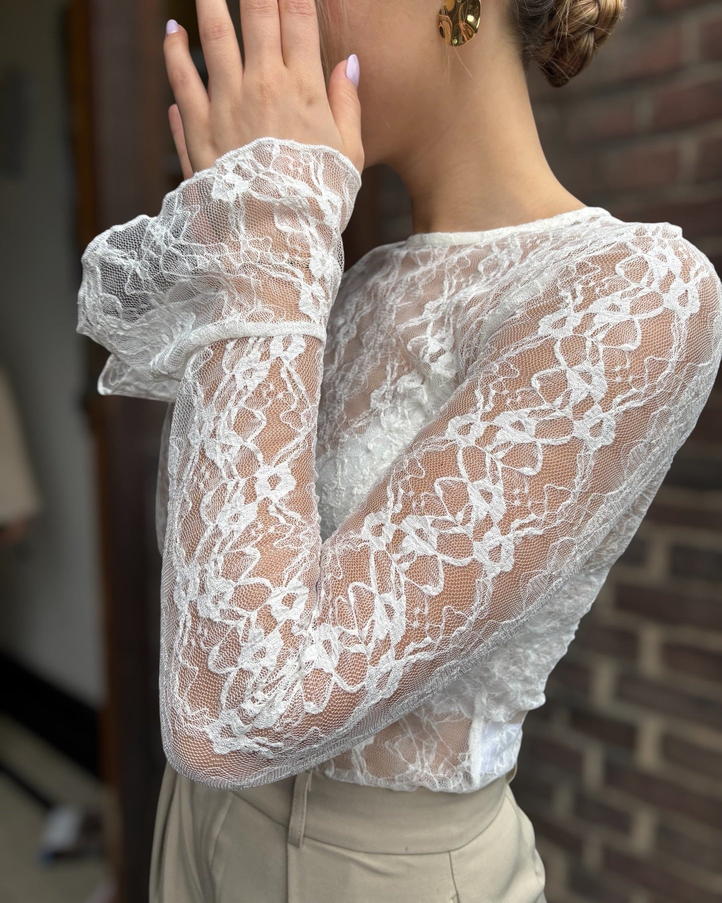 Blouse blanche en dentelles légère et transparente. Coupe moulante avec des longues manches évasées et une dentelle florale.