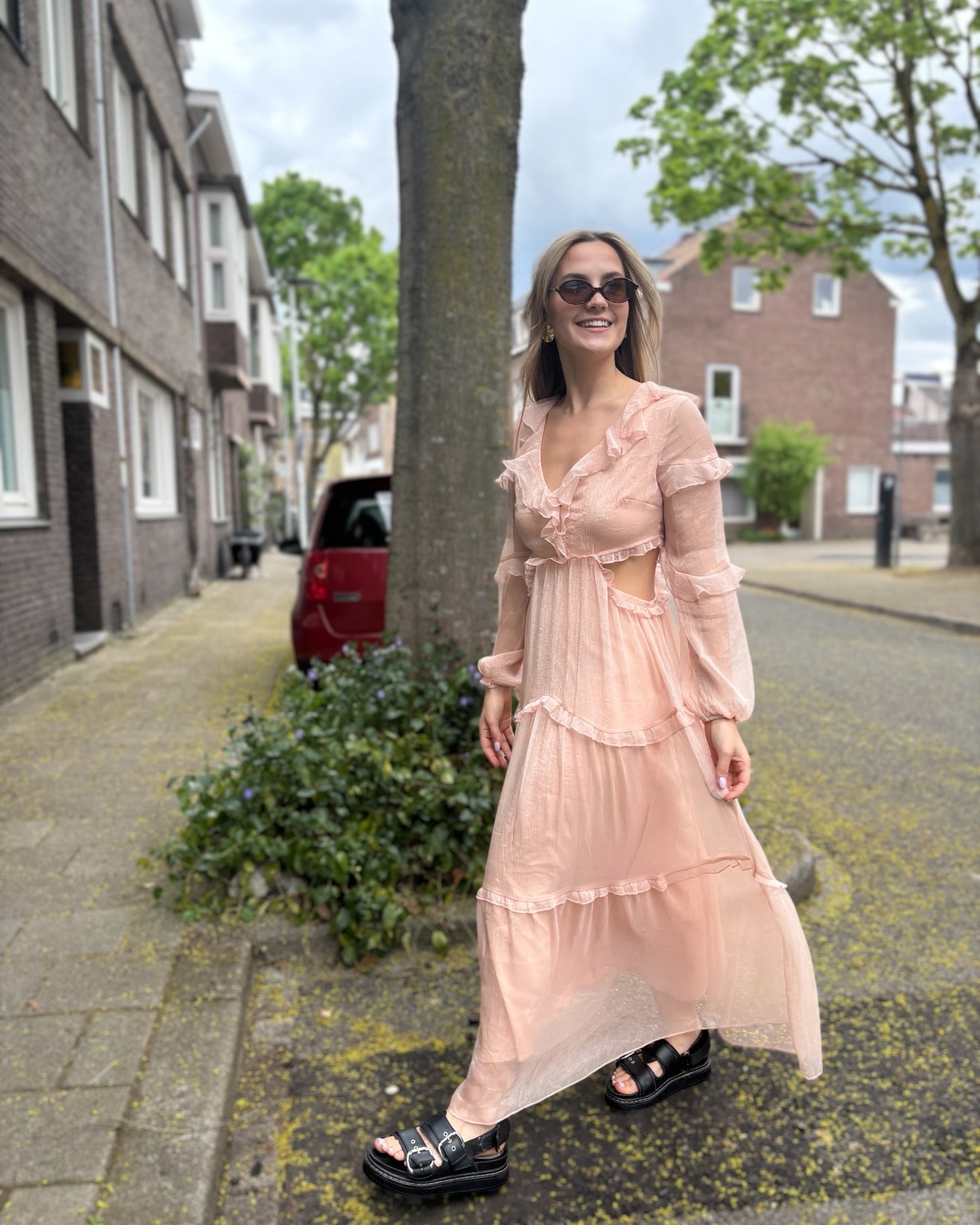 Robe rose longue doublée jusqu’aux cuisses. Décolleté en V avec petits volants. Détails ajourés sur les côtés.