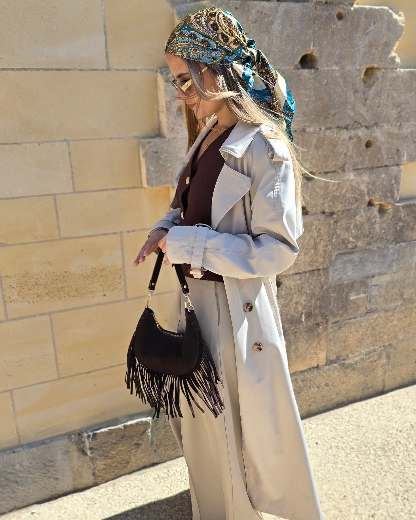 Trench beige coupe longue avec épaules structurées et une ceinture à nouer. Doublé intégralement. 