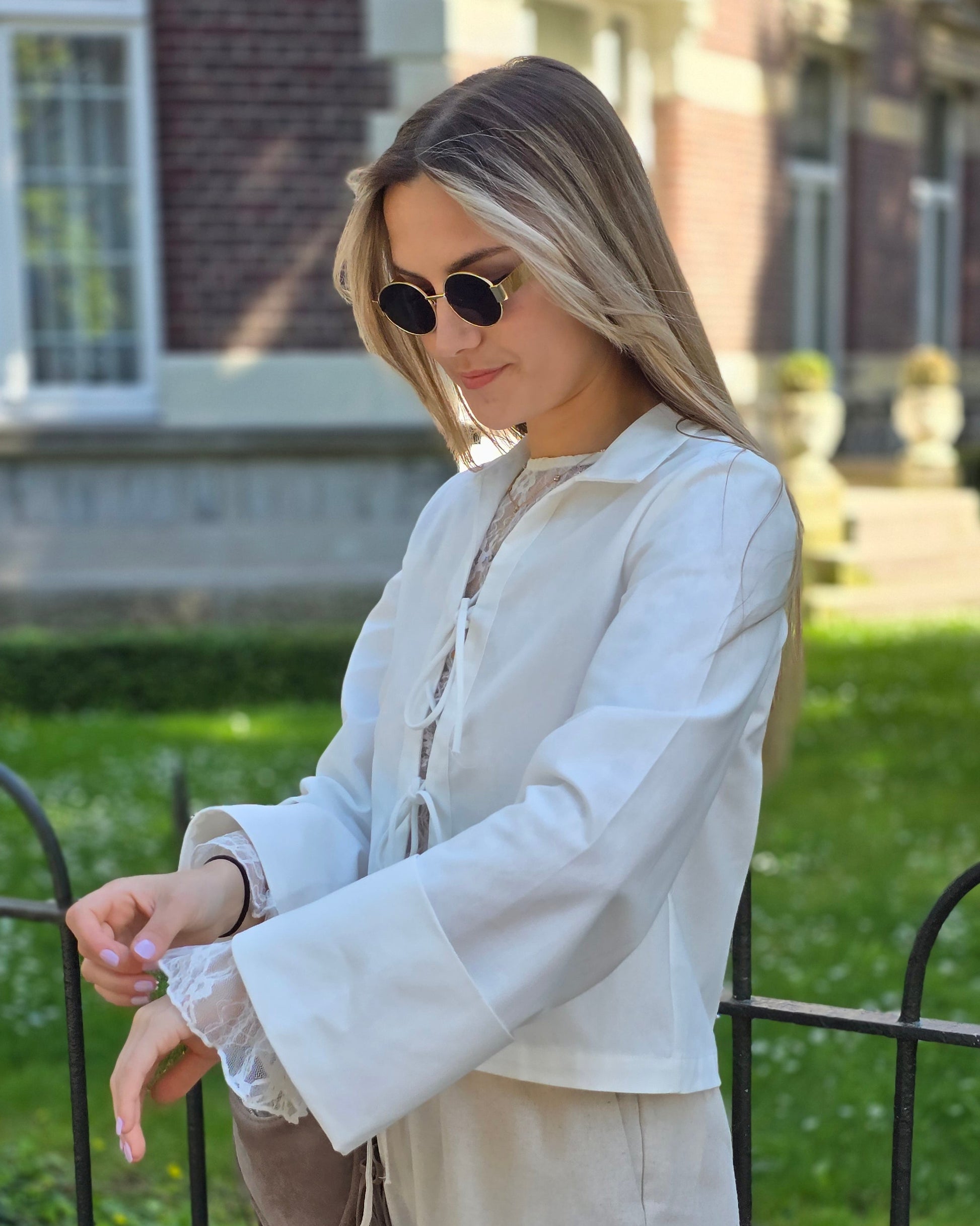 Blouse blanche en coton-lin à manches longues avec poignets larges. Coupe droite légèrement courte avec des liens à nouer à l’avant. 