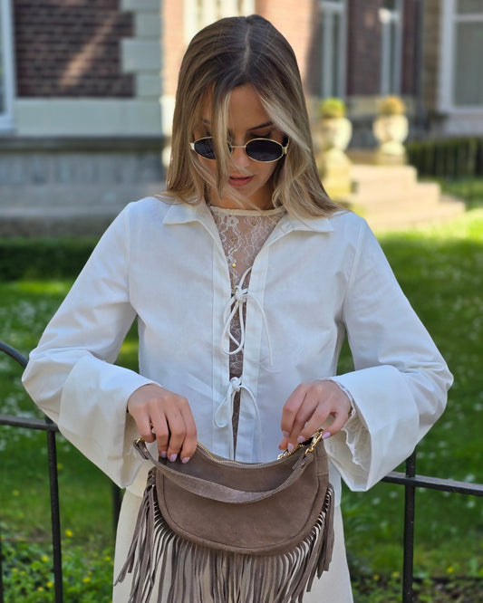 Blouse blanche en coton-lin à manches longues avec poignets larges. Coupe droite légèrement courte avec des liens à nouer à l’avant. 