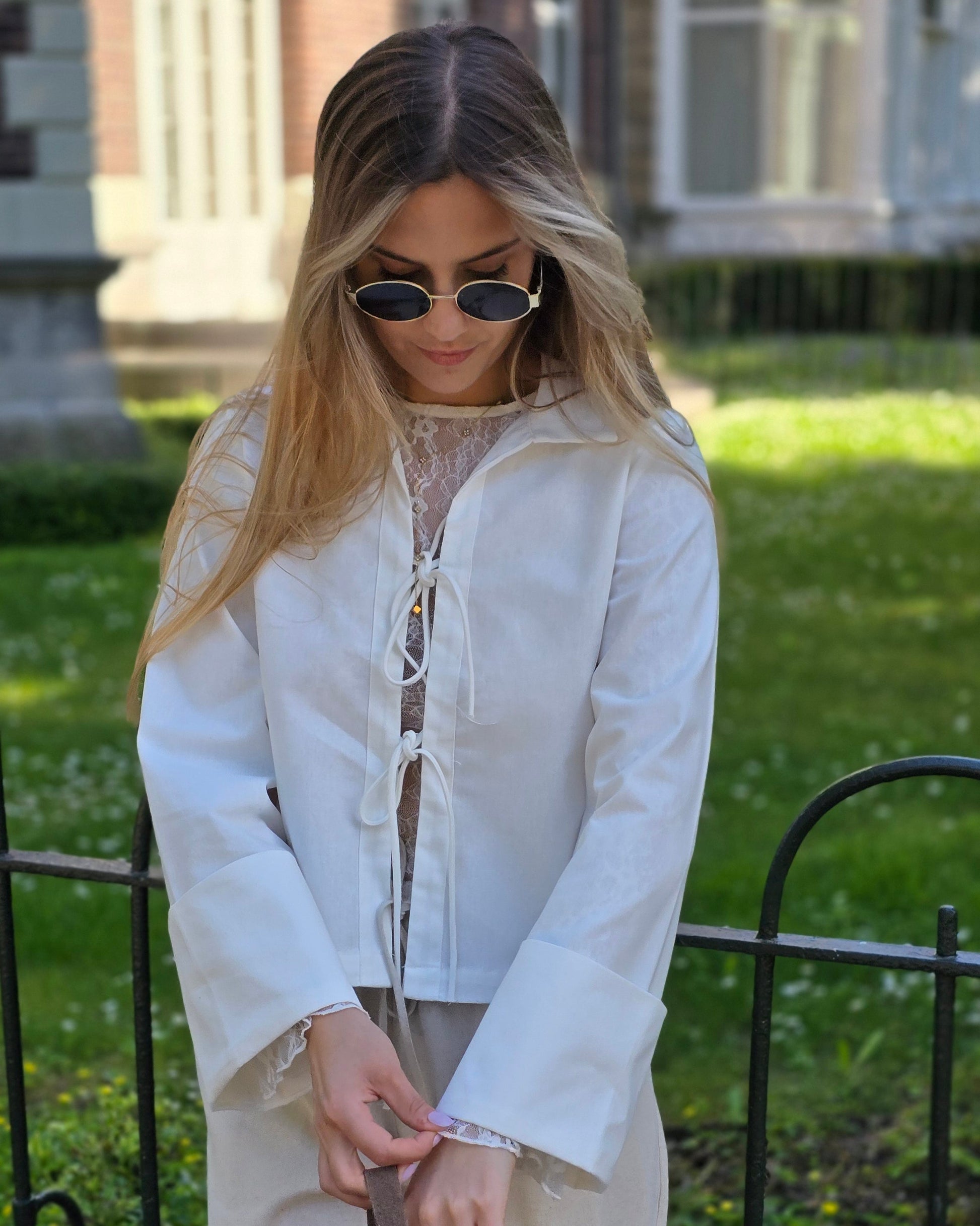 Blouse blanche en coton-lin à manches longues avec poignets larges. Coupe droite légèrement courte avec des liens à nouer à l’avant. 