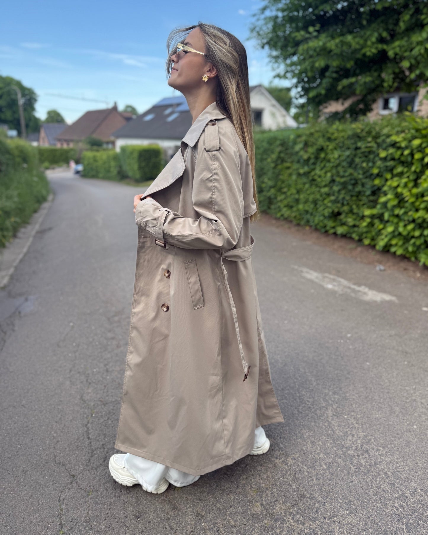 Trench taupe coupe longue avec épaules structurées et une ceinture à nouer. Doublé intégralement. 