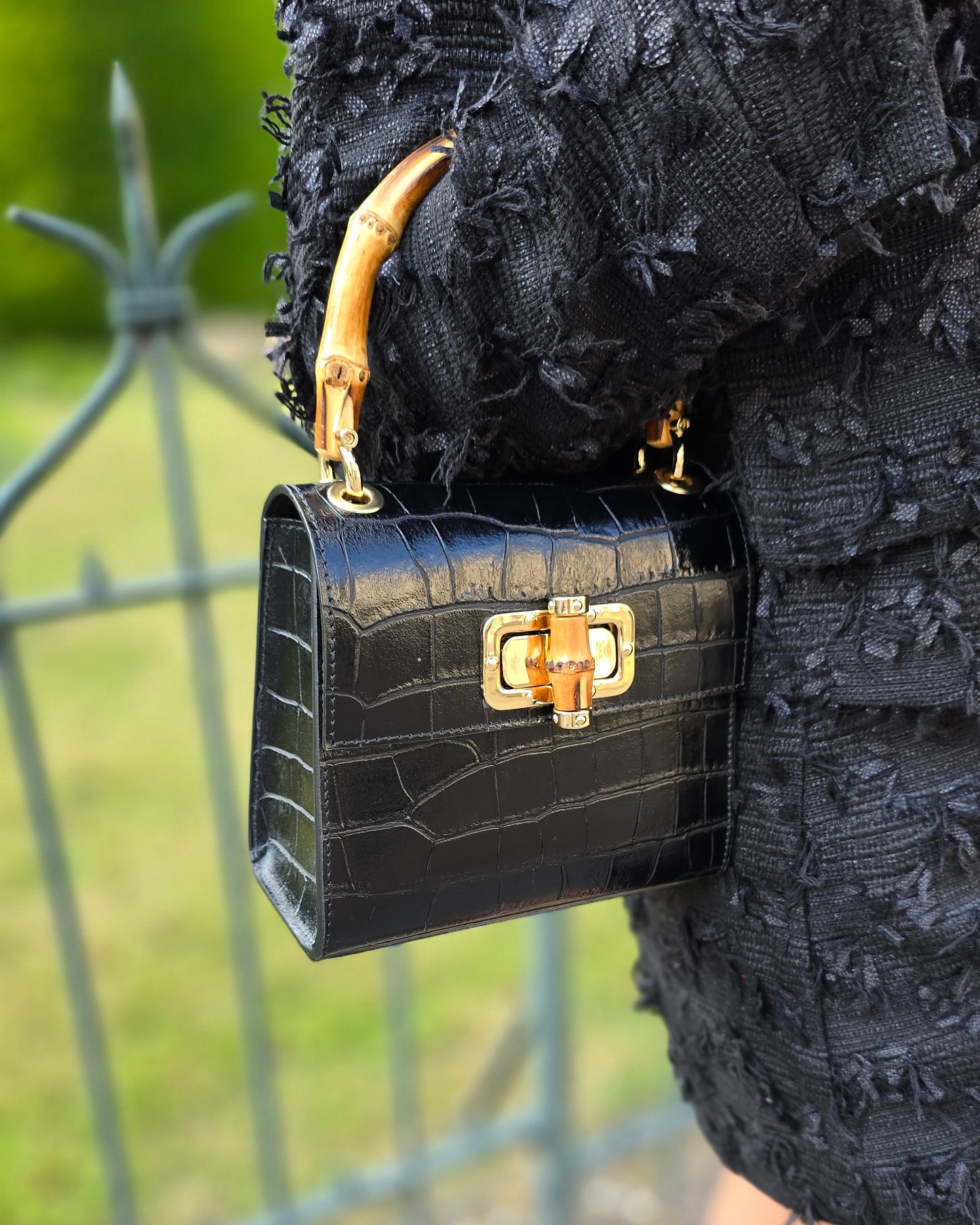 Petit sac à main noir en cuir et poignée en bamboo. Effet croco. Fermoire à l’avant. Sangle disponible. 