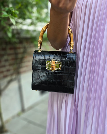 Petit sac à main noir en cuir et poignée en bamboo. Effet croco. Fermoire à l’avant. Sangle disponible. 
