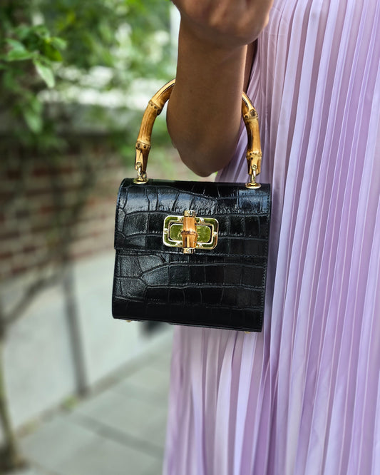 Petit sac à main noir en cuir et poignée en bamboo. Effet croco. Fermoire à l’avant. Sangle disponible. 