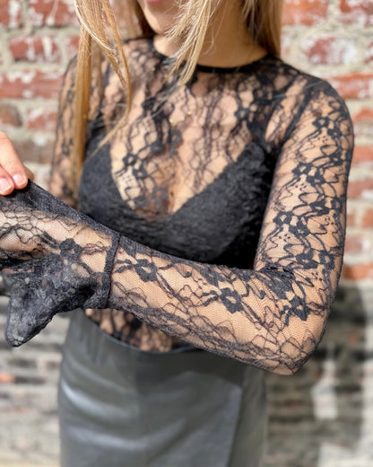 Blouse noire en dentelles légère et transparente. Coupe moulante avec des longues manches évasées et une dentelle florale. 
