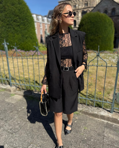 Blazer sans manches couleur noir. Deux fausses poches devant et fente à l’arrière.