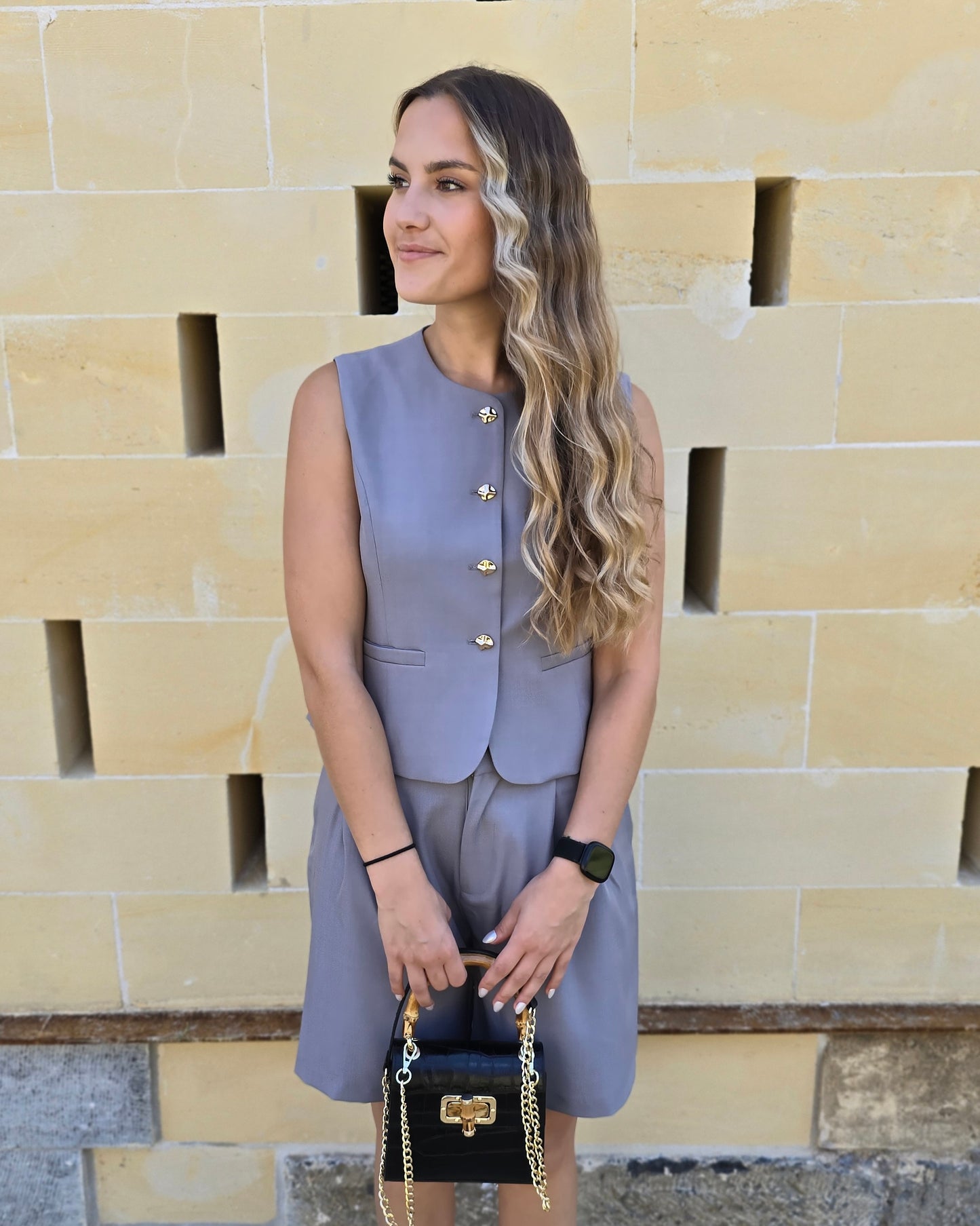 Top tailleur gris foncé avec boutons dorés. Effet cintré et fausses poches sur le devant. 