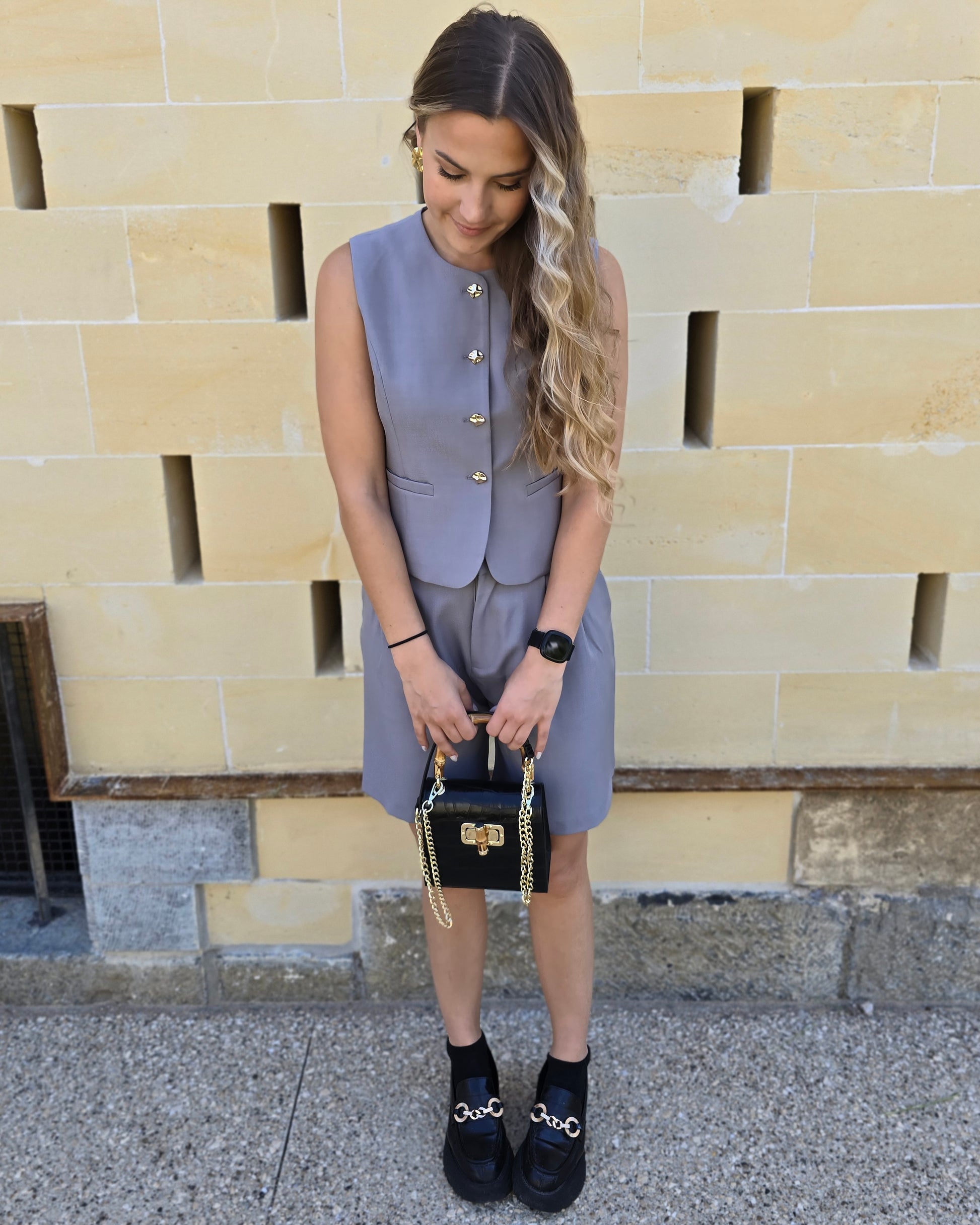 Top tailleur gris foncé avec boutons dorés. Effet cintré et fausses poches sur le devant. 