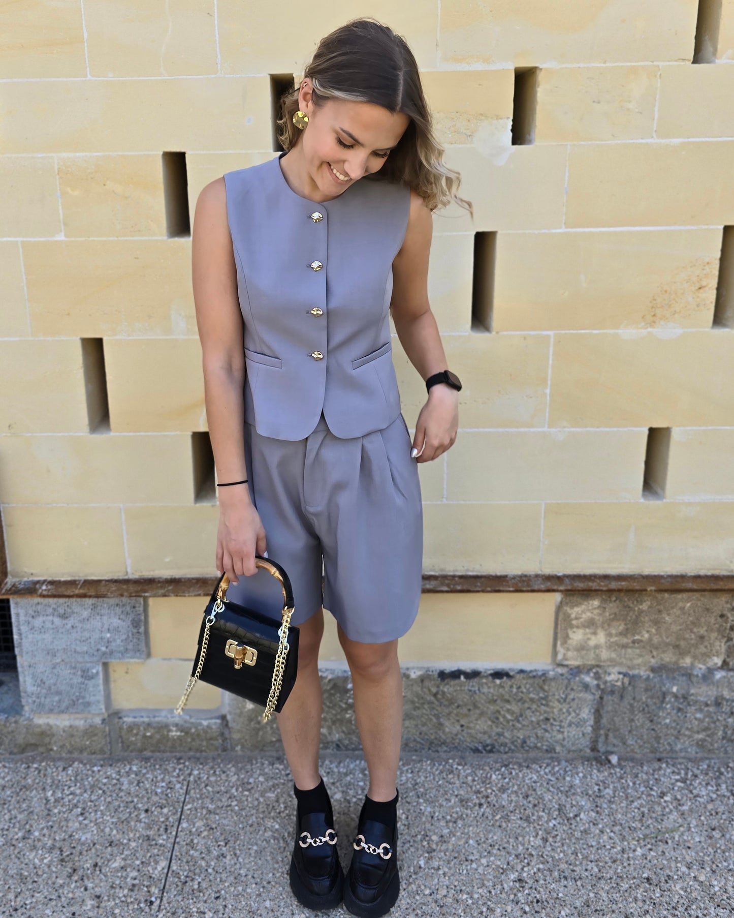 Bermuda gris foncé longueur genou. Avec des pinces à l’avant et deux poches. Ensemble tailleur