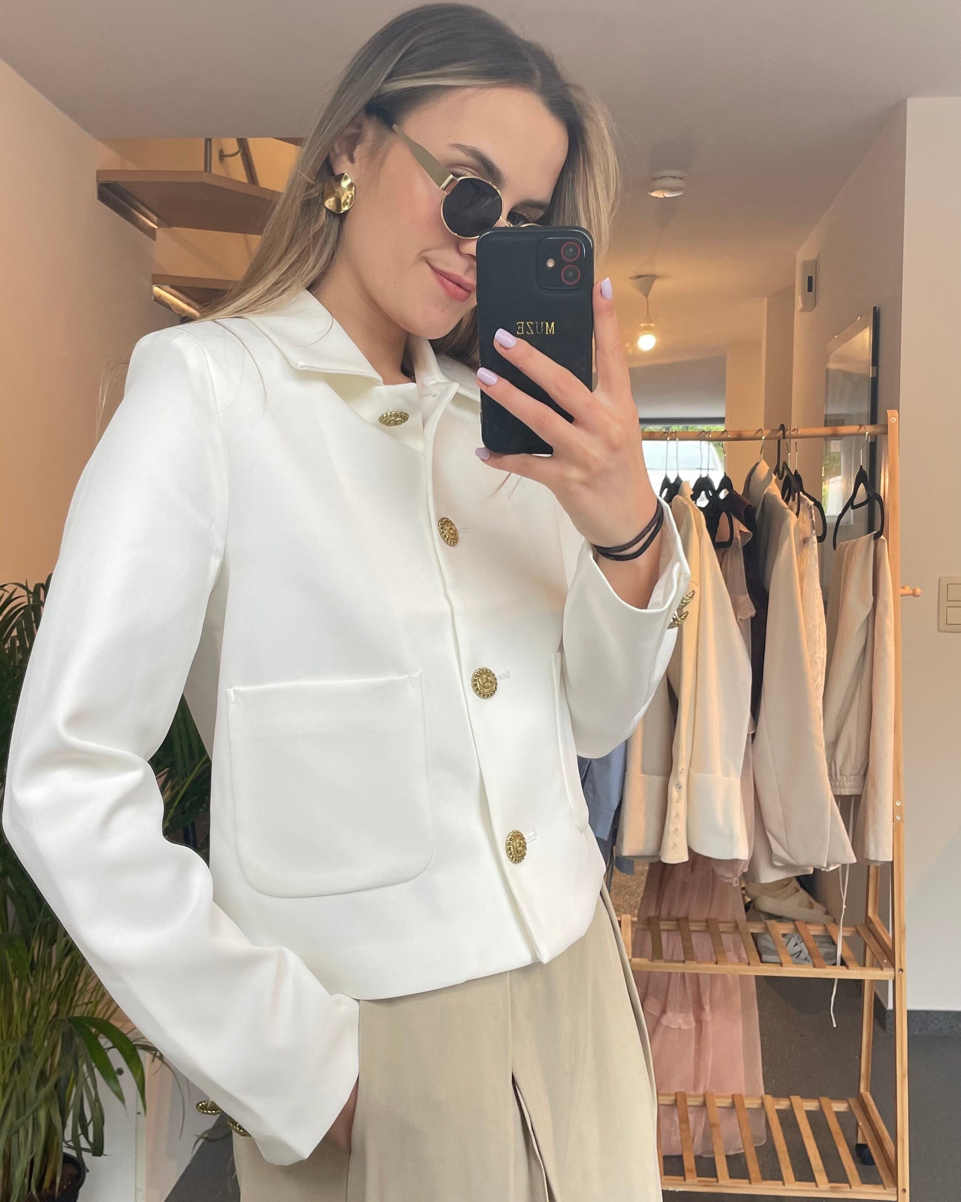Veste blanche tailleur. Coupe droite légèrement cintrée. Fermeture avec des boutons dorés gravés et deux grandes poches à l’avant. 