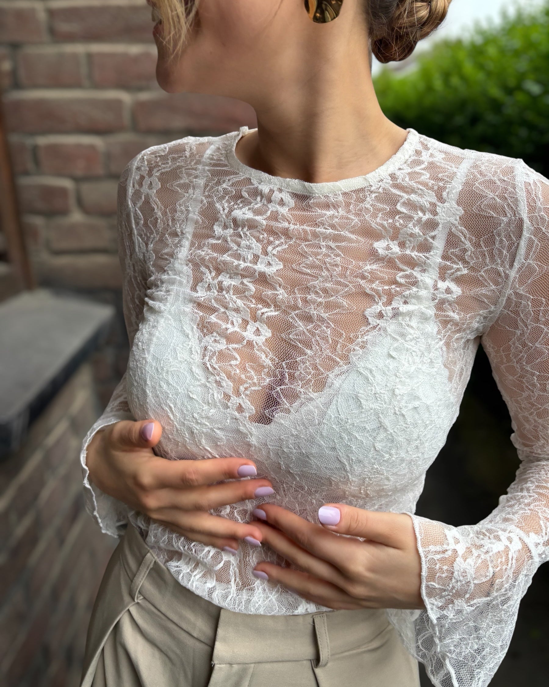 Blouse blanche en dentelles légère et transparente. Coupe moulante avec des longues manches évasées et une dentelle florale. 