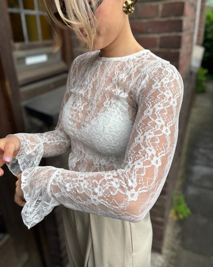 Blouse blanche en dentelles légère et transparente. Coupe moulante avec des longues manches évasées et une dentelle florale. 