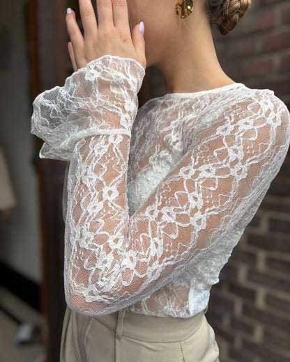Blouse blanche en dentelles légère et transparente. Coupe moulante avec des longues manches évasées et une dentelle florale. 