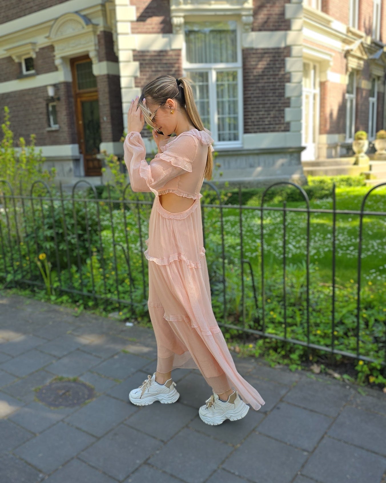 Robe rose longue doublée jusqu’aux cuisses. Décolleté en V avec petits volants. Détails ajourés sur les côtés. 