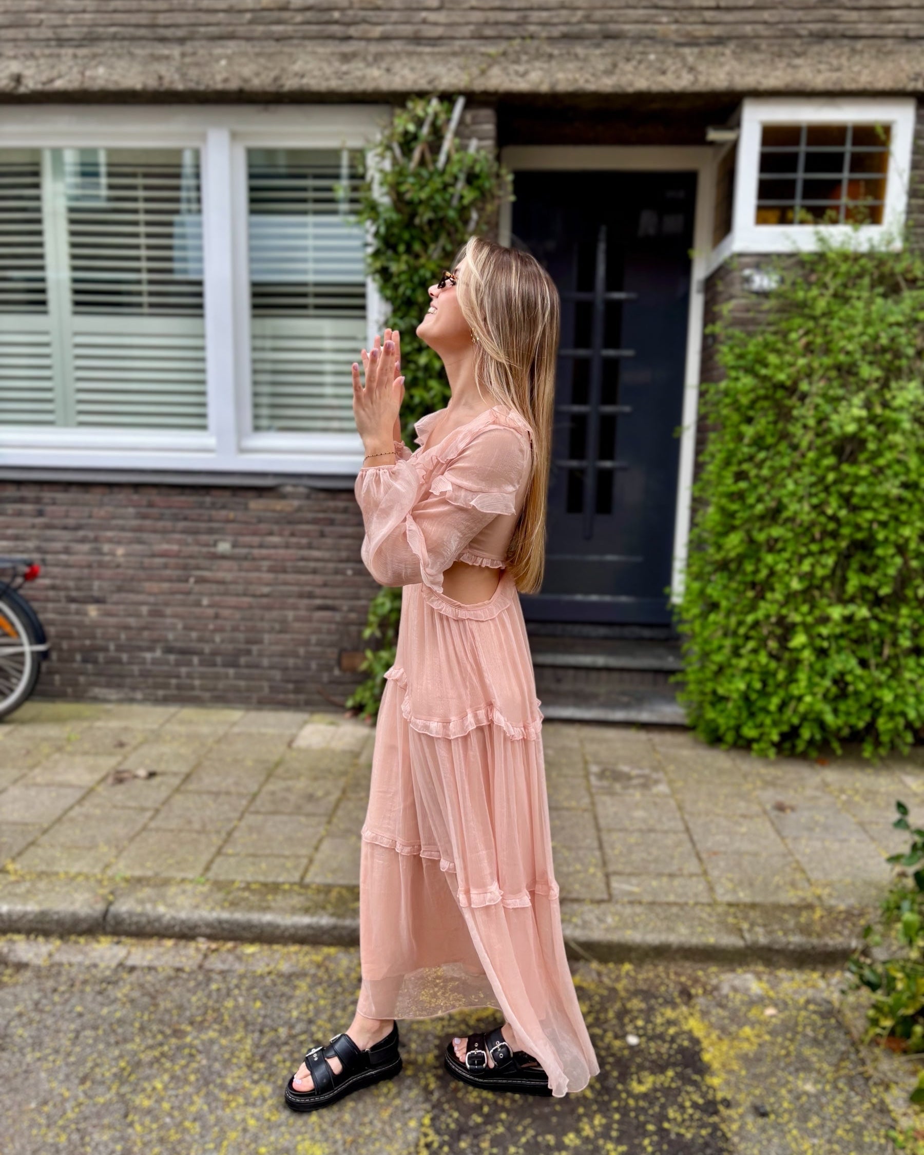 Robe rose longue doublée jusqu’aux cuisses. Décolleté en V avec petits volants. Détails ajourés sur les côtés. 