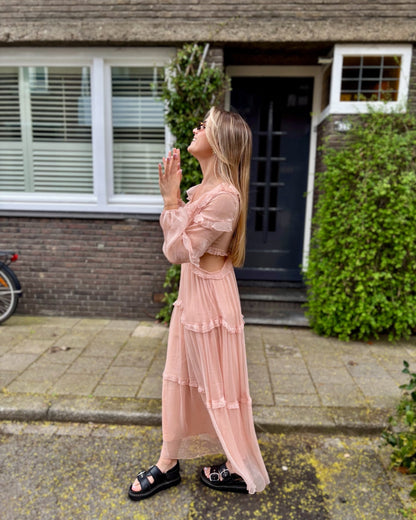 Robe rose longue doublée jusqu’aux cuisses. Décolleté en V avec petits volants. Détails ajourés sur les côtés. 