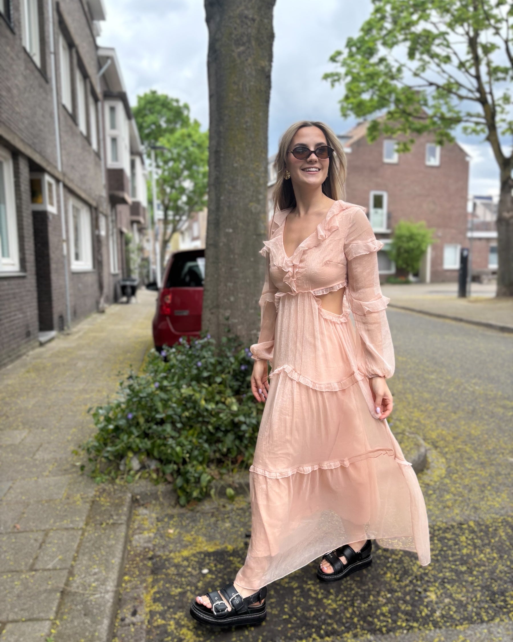 Robe rose longue doublée jusqu’aux cuisses. Décolleté en V avec petits volants. Détails ajourés sur les côtés. 