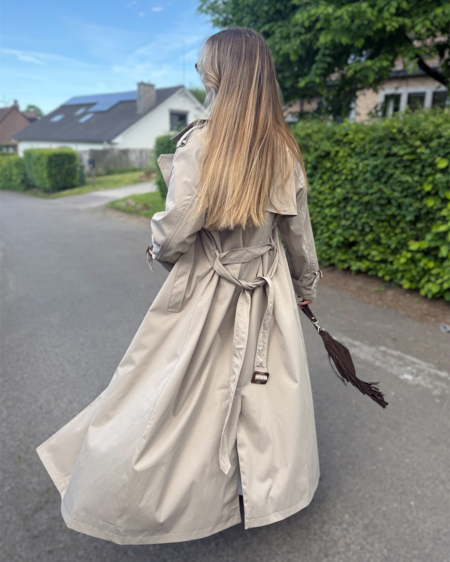 Trench taupe coupe longue avec épaules structurées et une ceinture à nouer. Doublé intégralement. 