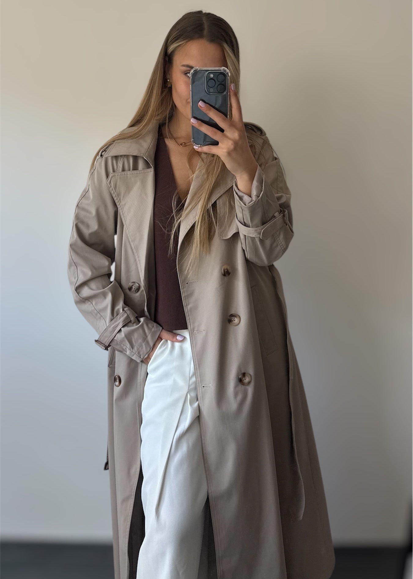 Trench taupe coupe longue avec épaules structurées et une ceinture à nouer. Doublé intégralement. 