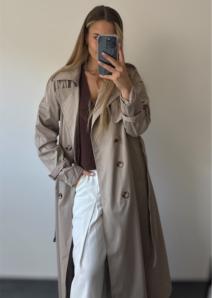 Trench taupe coupe longue avec épaules structurées et une ceinture à nouer. Doublé intégralement. 