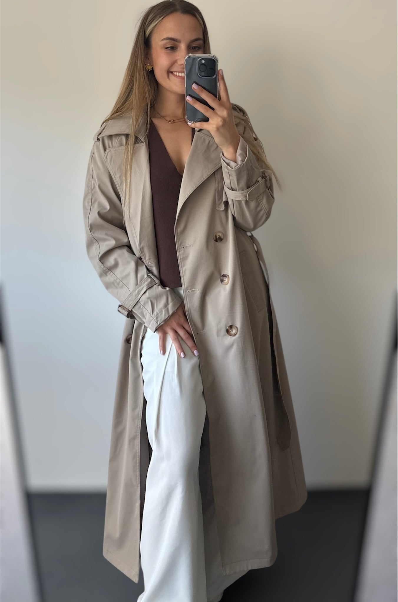 Trench taupe coupe longue avec épaules structurées et une ceinture à nouer. Doublé intégralement. 