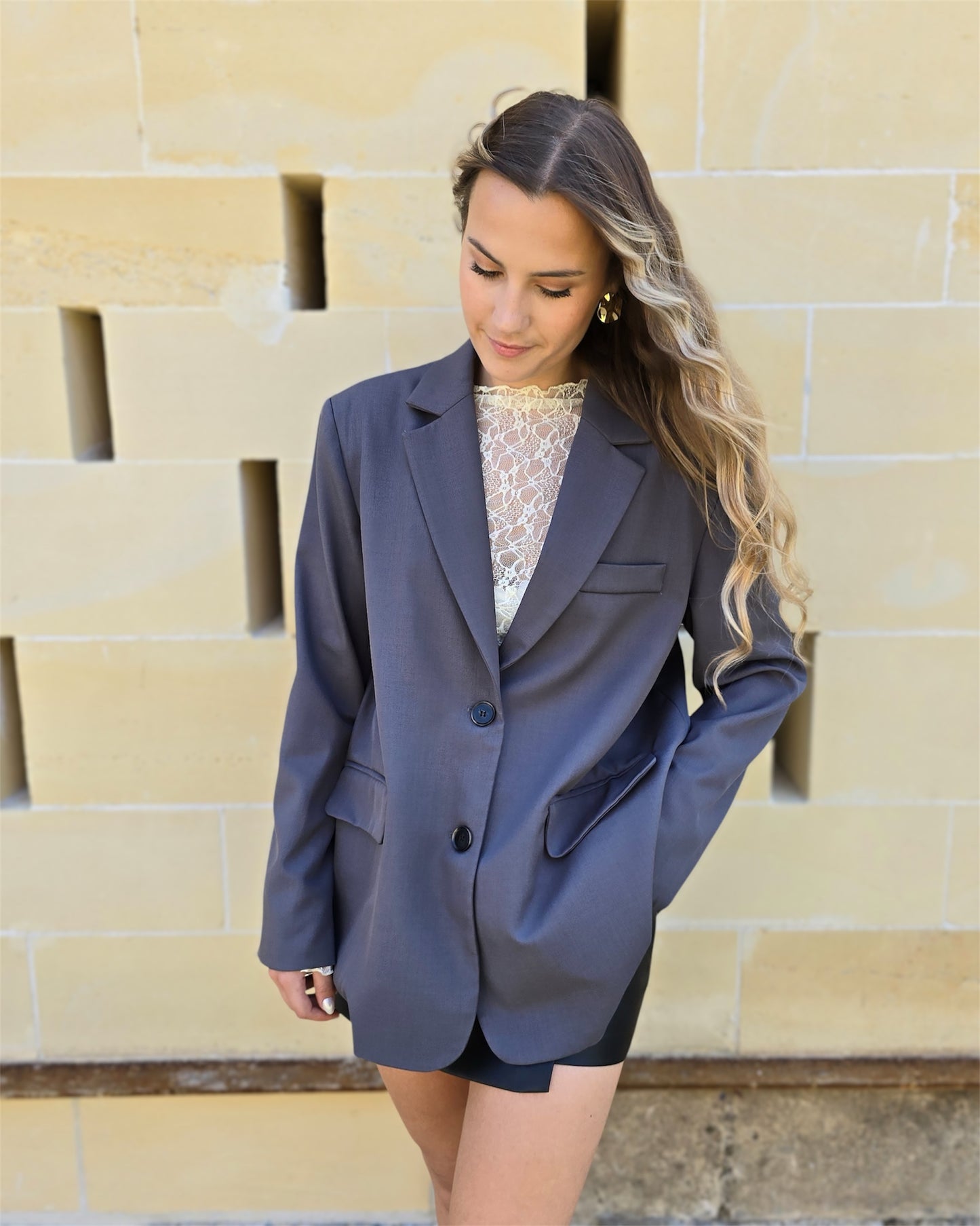 Blazer gris oversize avec ouverture dans le dos. Deux boutons à l’avant et deux fausses poches. 