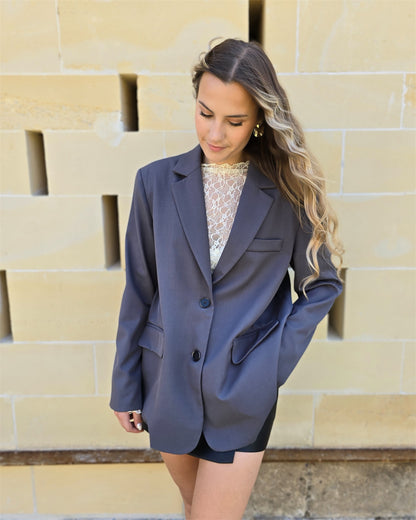 Blazer gris oversize avec ouverture dans le dos. Deux boutons à l’avant et deux fausses poches. 