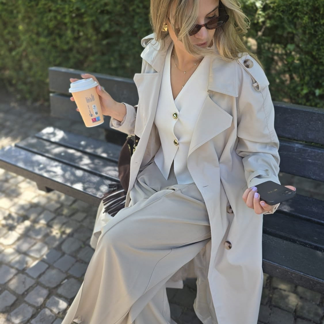Trench beige coupe longue avec épaules structurées et une ceinture à nouer. Doublé intégralement. 